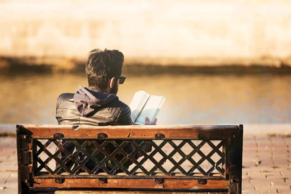 A guy reading a book on a bench