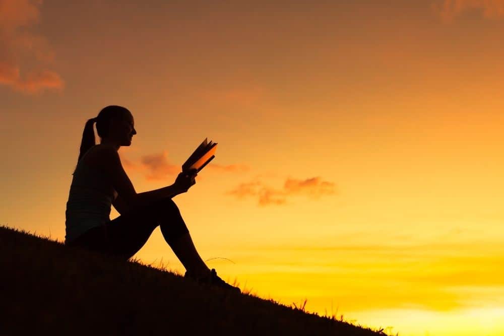 A girl reads on a hill at sunset