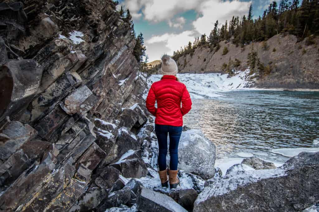 A woman stands on the shore looking at Bow Falls in Banff